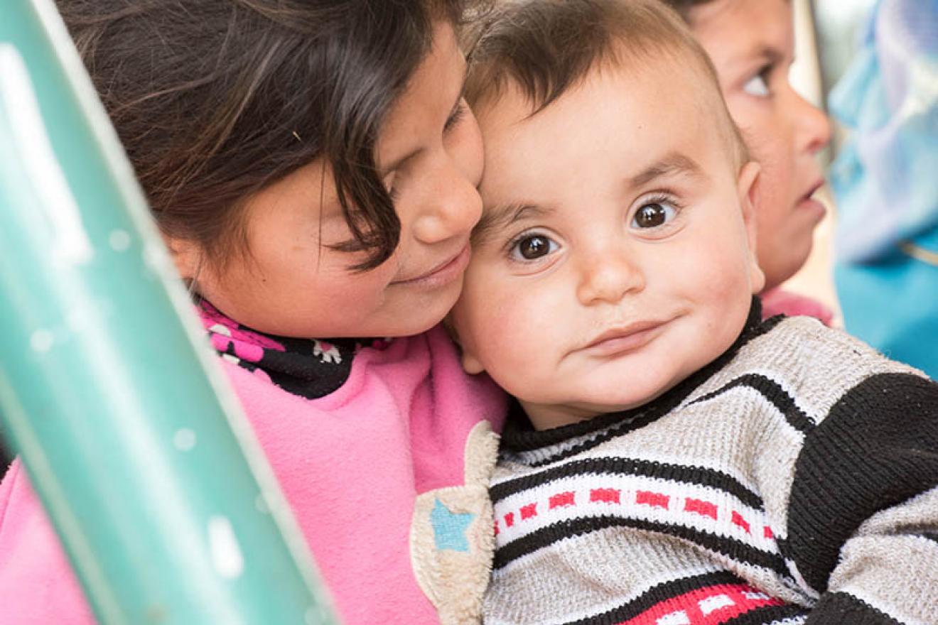 A young girl holds a smiling infant at the Zaatari Refugee Camp