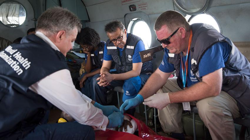 A helicopter transports a wounded health worker and others, while Dr. Michael Ryan helps tend to him.