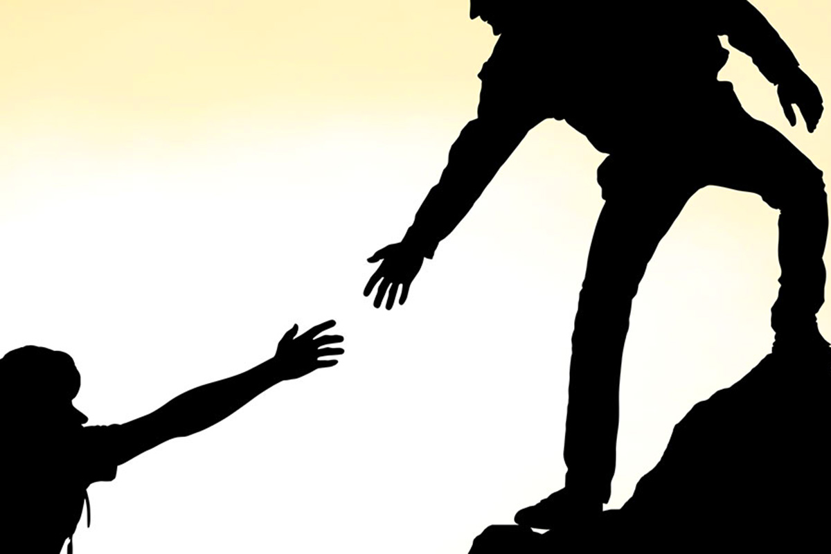 The silhouettes of a person reaching down to help another.