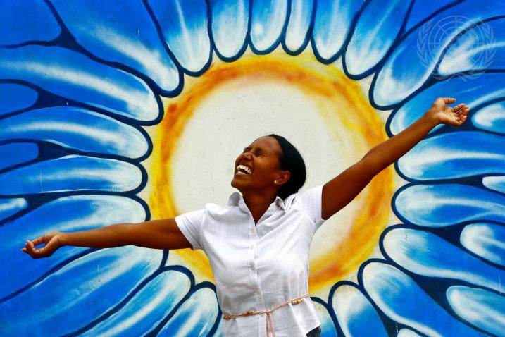 在纪念世界精神卫生日之际，一名妇女在代表太阳的涂鸦前摆出姿势，摄于东帝汶帝力。联合国图片/Martine Perret