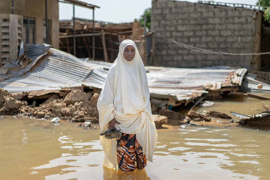 Woman standing in flood water in front of house destroyed by flood